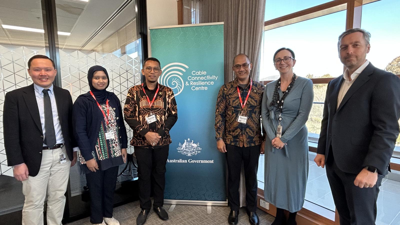 CCRC and Indonesian representatives standing together in an office beside a CCRC banner during the undersea cable resilience study tour.