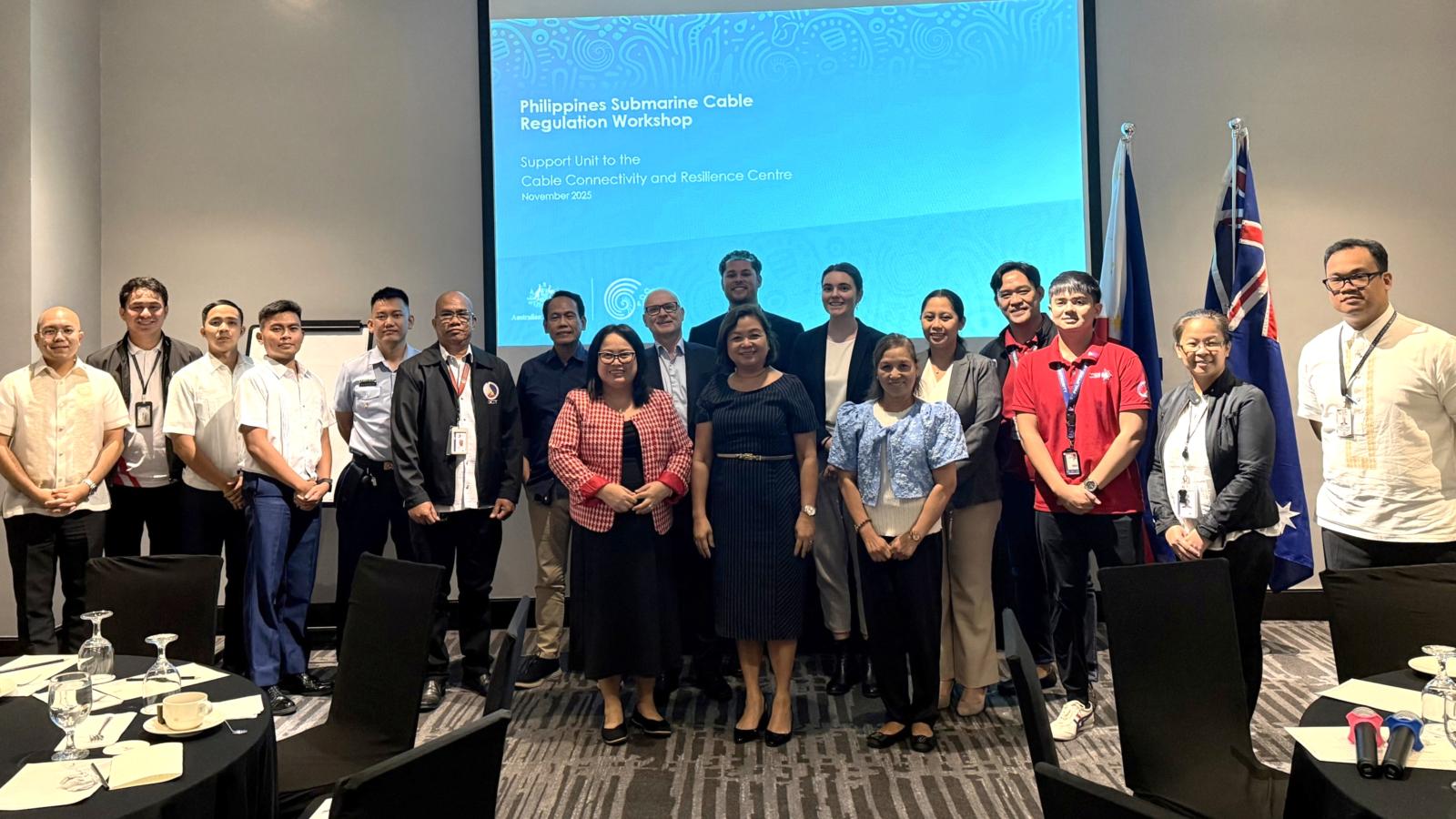 Participants stand in a conference room in front of a projector screen for a workshop in the Phiippines on the protection and strengthening of subsea telecommunications cables. 