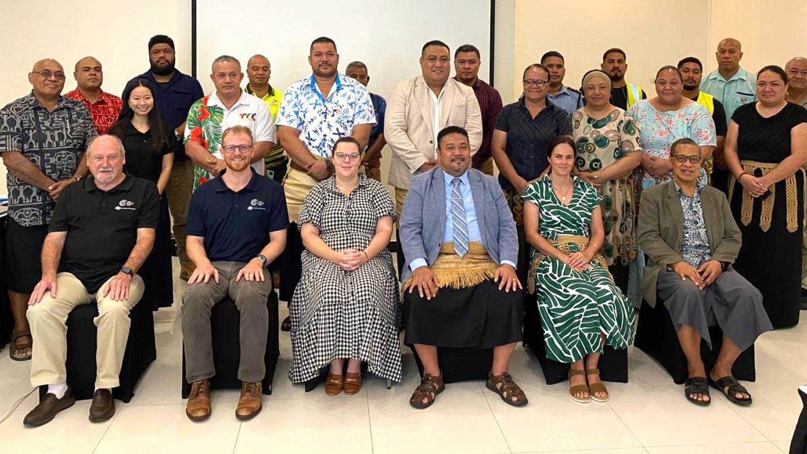 A formal group photo of attendees standing and sitting at meeting in Tonga to discuss  telecommunications. 